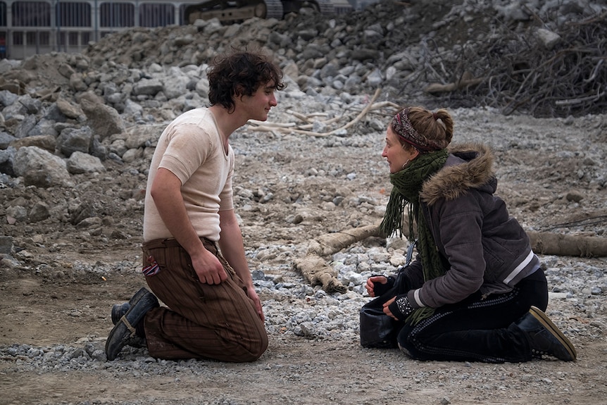 Colour still of Alba Rohrwacher and Adriano Tardiolo kneeling and facing each other amongst rubble in film Happy as Lazzaro.