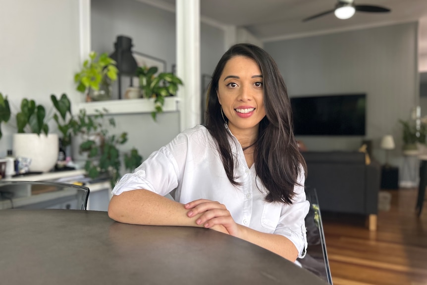 A woman sitting at a table smiles at the camera.