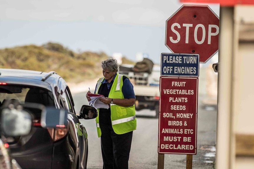 A woman standing next to a car holding a clipboard while talking to the driver through the open car window.