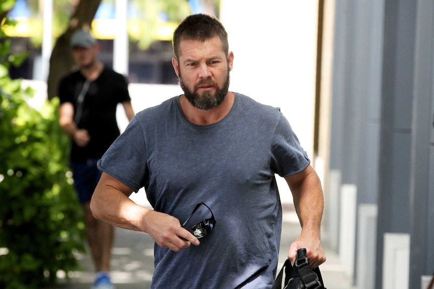 A mid shot of Ben Cousins walking outside a building wearing a blue t-shirt.