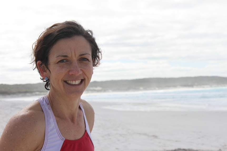 A smiling woman wearing bathers, standing on the beach