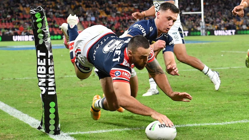 A Roosters player is mid-air as his hand plants the ball down in the corner for a try.