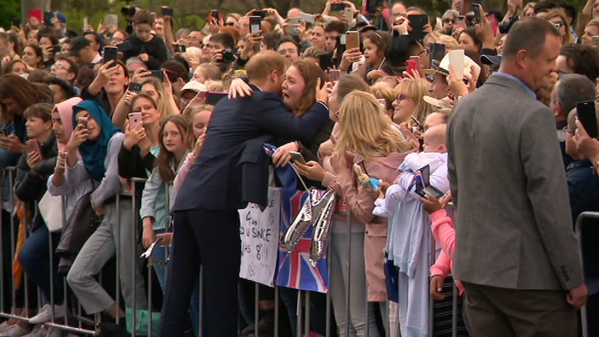 Prince Harry hugs a woman as she bursts into tears in a crowd of people.