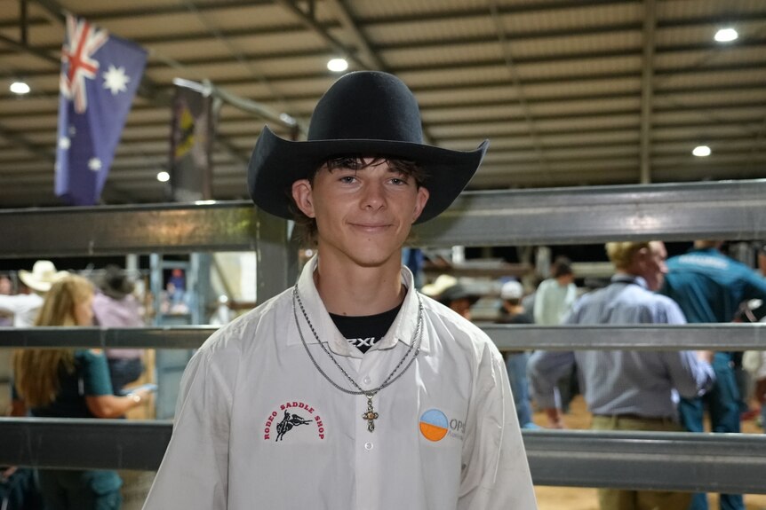 a 16-year-old bullrider poses in front of the ring wearing a large black cowboy hat