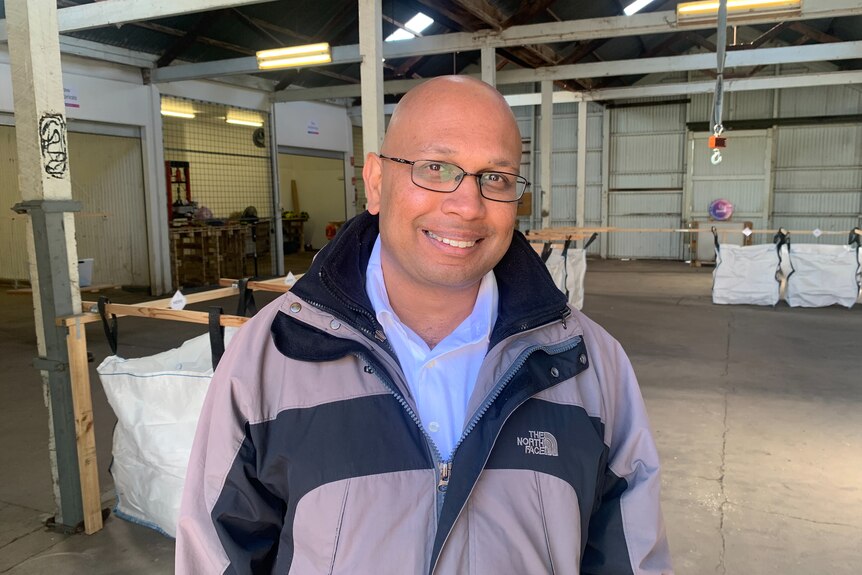 A bald man in glasses smiles at the camera in a factory.