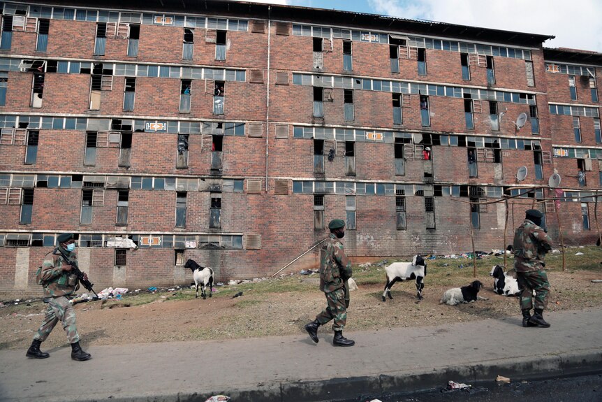 South African soldiers walk past decrepit looking buildings and goats