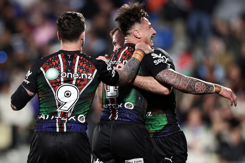Three Warriors NRL players embrace as they celebrate a try against the Sharks.