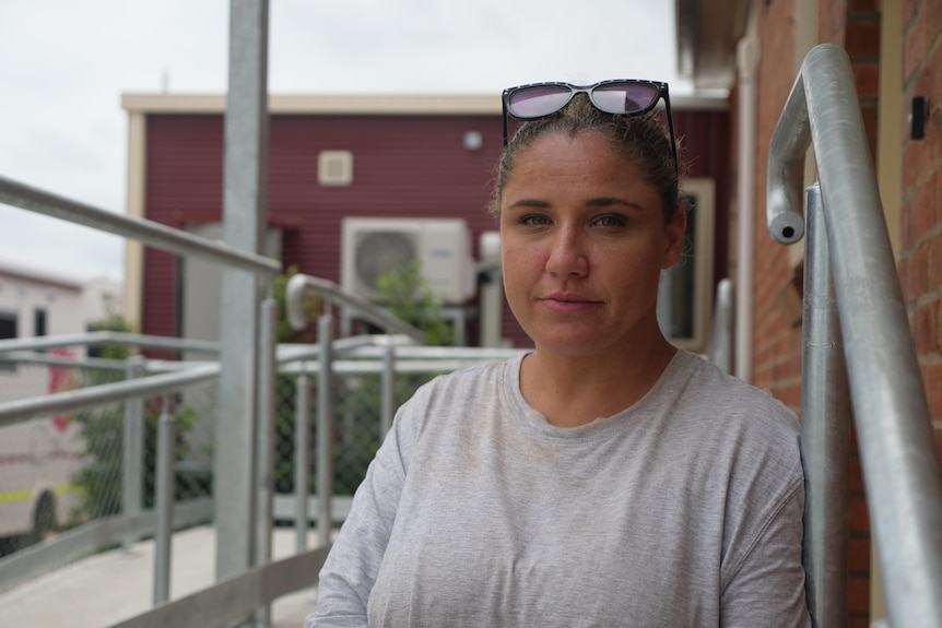 A woman in a grey shirt with sunglasses on her head sitting on cement stairs