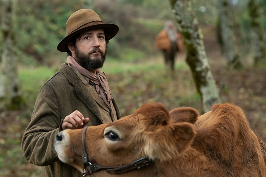 Film still of John Magaro as Cookie with a cow in First Cow