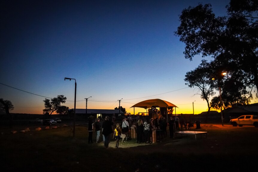 People gather at a playground in a town camp with a sunset unfolding in the background