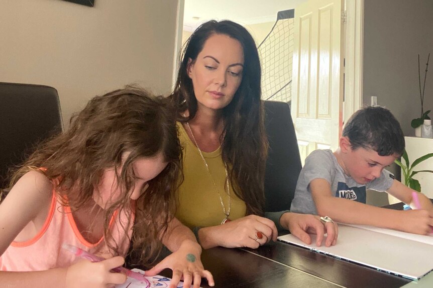 woman sits with children at table as they draw