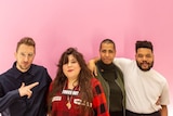 Four artists are arm-in-arm as they pose in front of a pale pink backdrop with the Turner Prize logo.