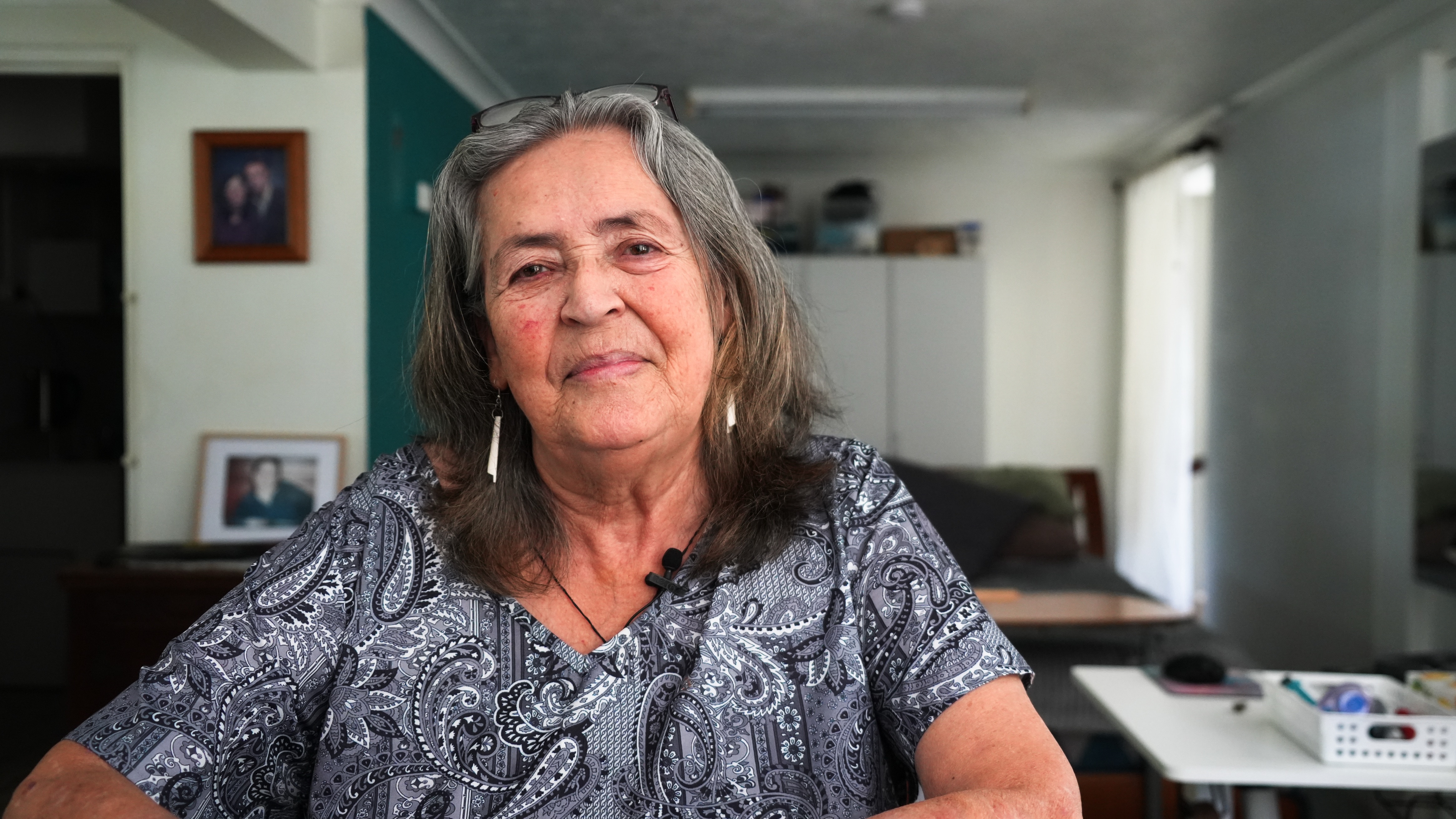 elderly lady with long grey hair sits and looks pensively at camera