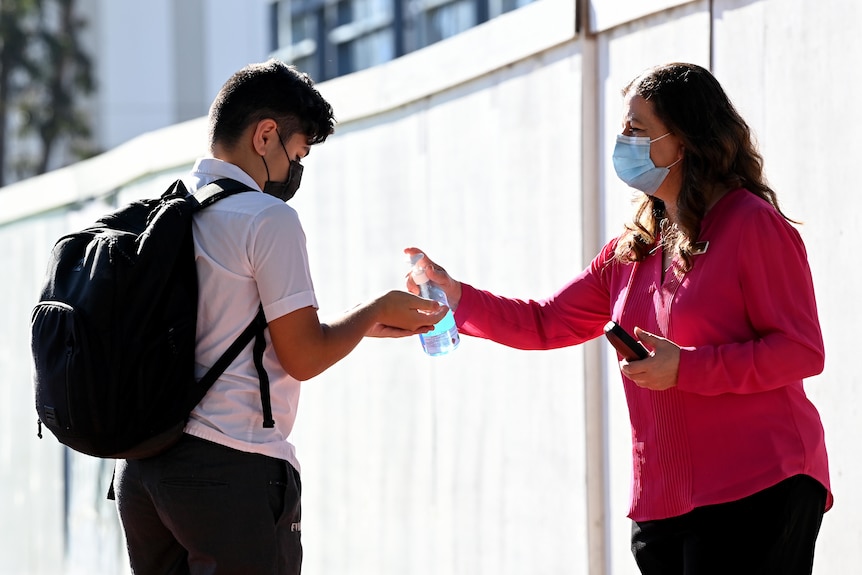 a student gets hand sanitiser sprayed on his hand by a woman wearing a mask