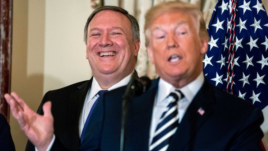 Mike Pompeo wears a big grin on his face as he stands behind Donald Trump, gesturing with his right hand, mid-speech