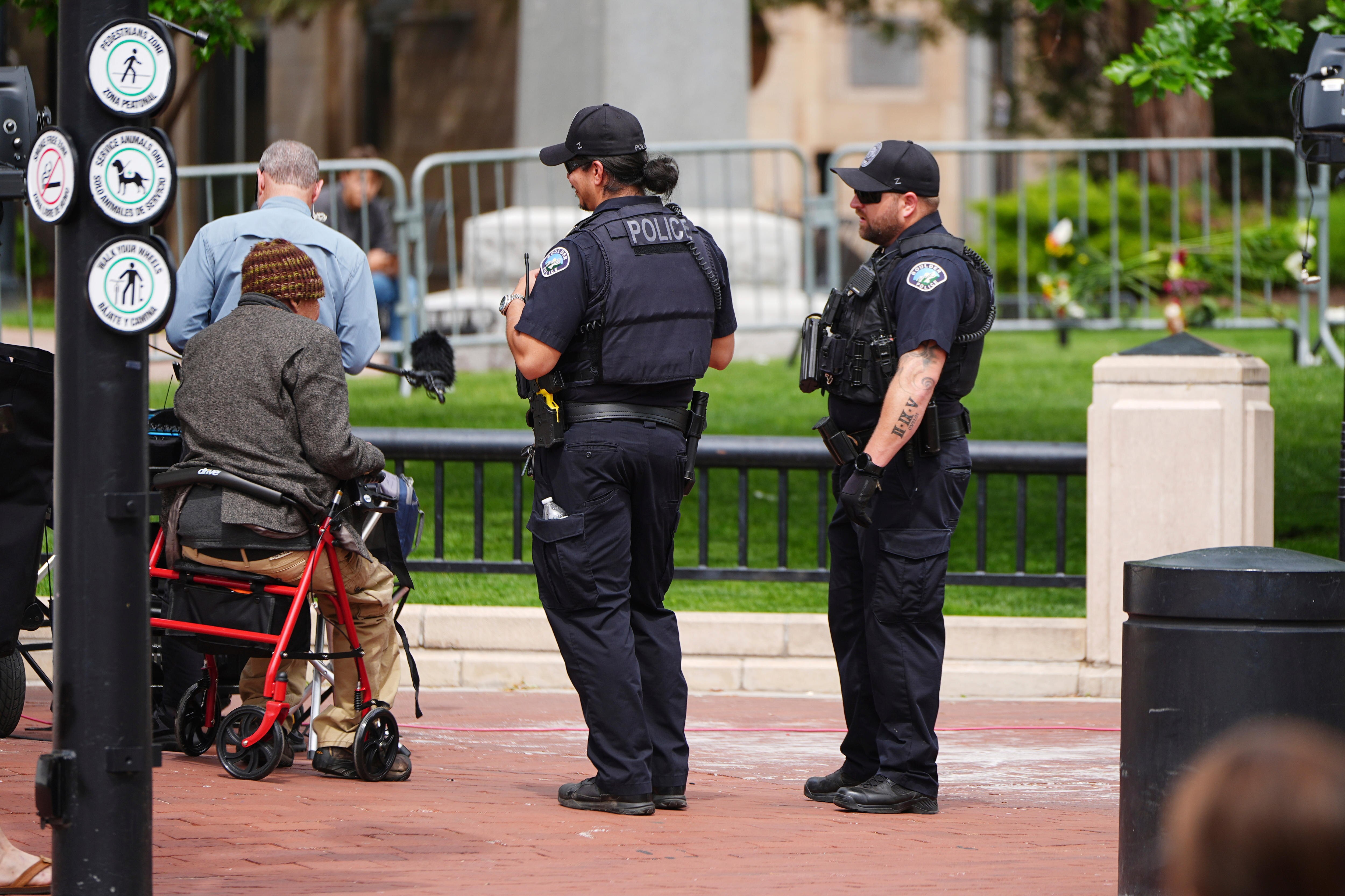 Two US police officers in black protective clothing speaking with a person wearing a beanie sitting in an assistance chair