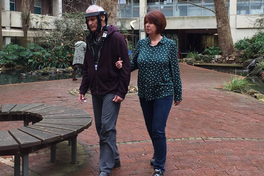 A man in a neck brace walks alongside a woman.