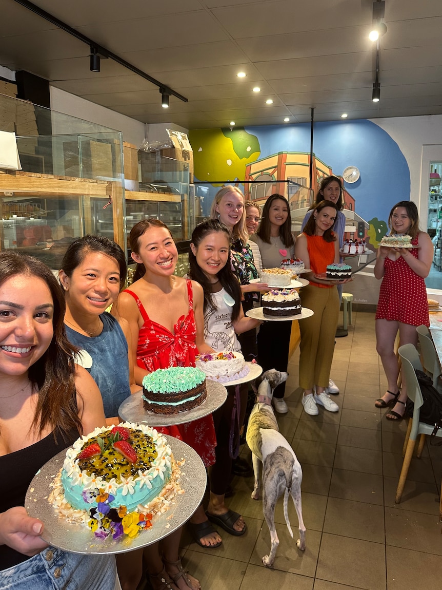 A row of young women hold up colourful cakes. 