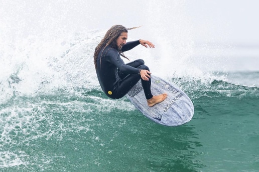 Man with long hear turning at the top of a wave on a white and grey board