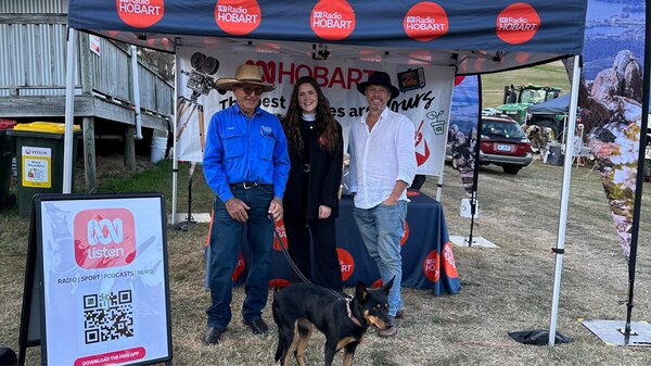 ABC staff stand under ABC Hobart branded marquee at Bream Creek show with dog