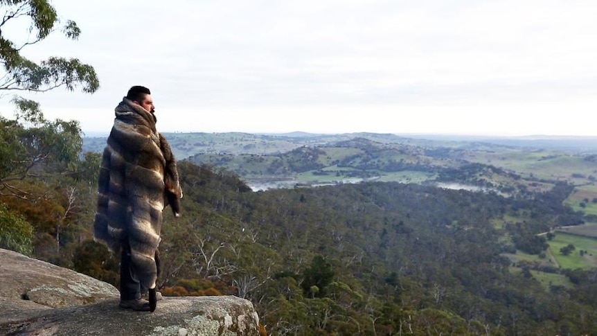 Indigenous man wears traditional coat and looks out over valley