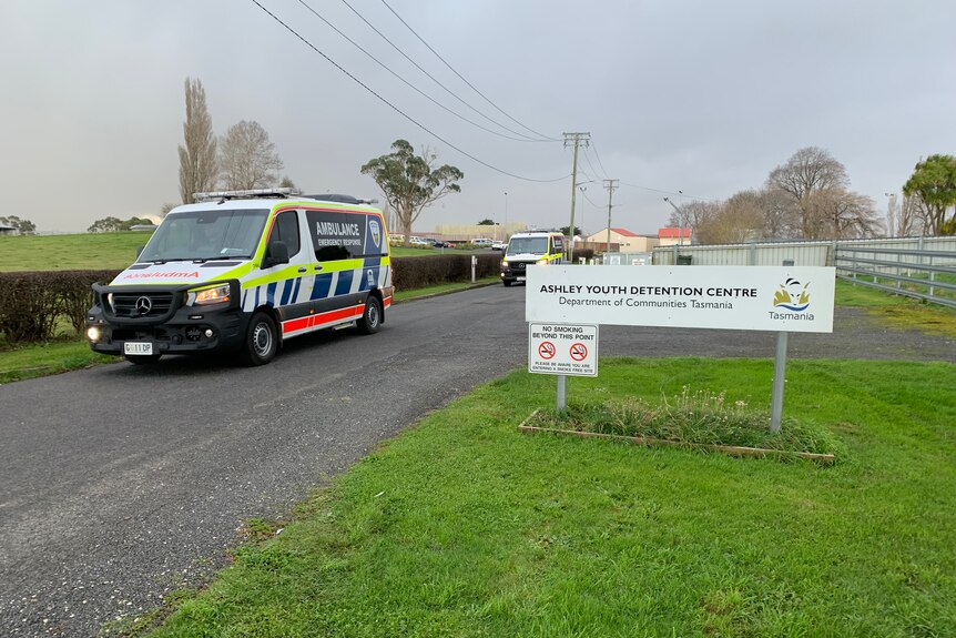 Two ambulances travel on a road past a sign saying: Ashley Youth Detention Centre