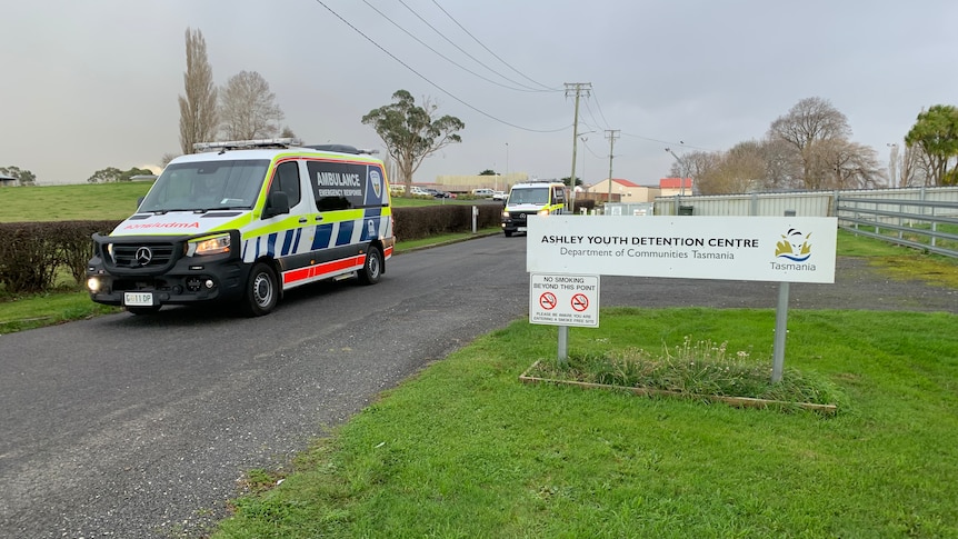 Two ambulances travel on a road past a sign saying: Ashley Youth Detention Centre