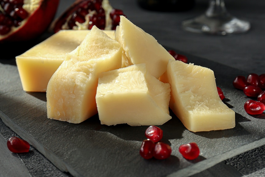 Chunks of hard chees on a dark stone platter, surrounds by kernels of pomegranate. 
