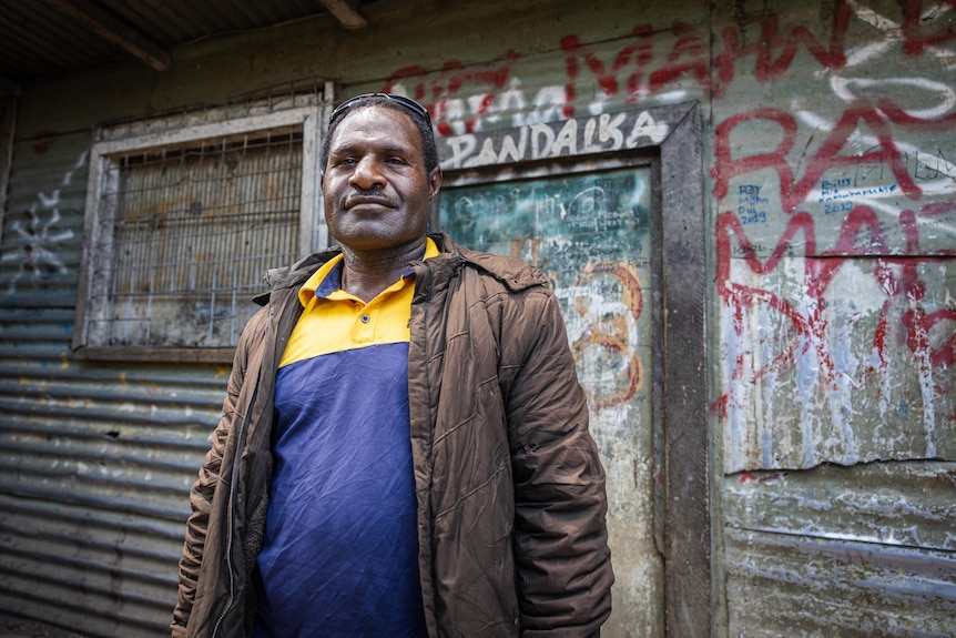 A Papua New Guinean man stands in front of a rundown metal building