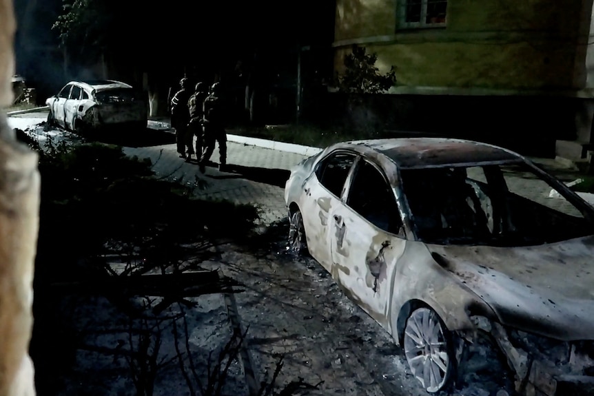 Police officers in a dark street next to damaged cars. 