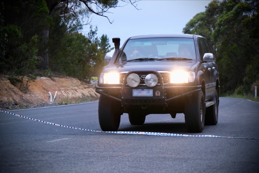 A car drives over police tape along a rural road.