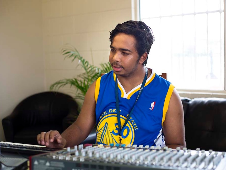 A young man sits in front a music desk and computer