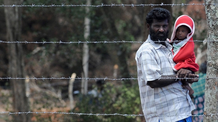 A Sri Lankan refugee father and his child stand behind barbed wire