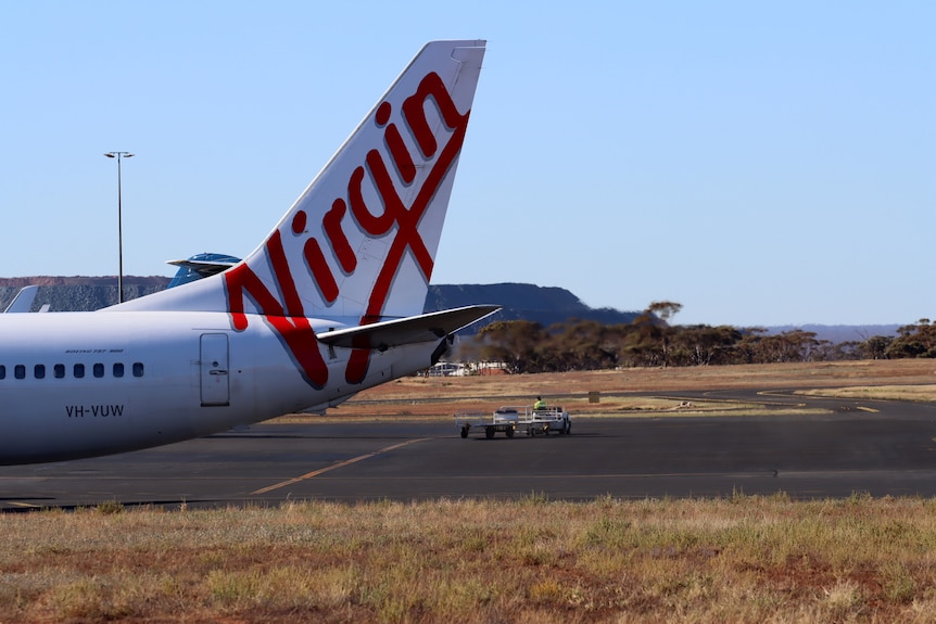 The tail of a Virgin plane showing insignia on a dry regional airport tarmac.