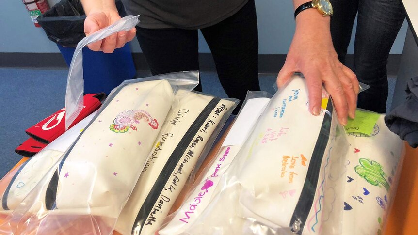 Stack of white pencil cases with inspirational notes written on them by school students, which hold prosthetic hands.