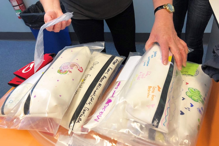 Stack of white pencil cases with inspirational notes written on them by school students, which hold prosthetic hands.