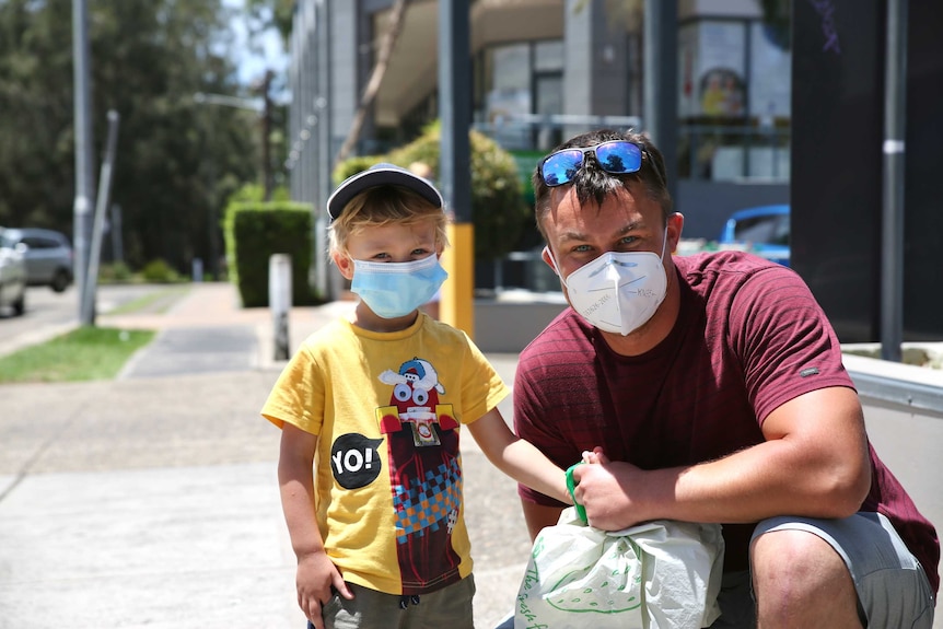 A young blonde child in a mask with a man bobbing down to his height