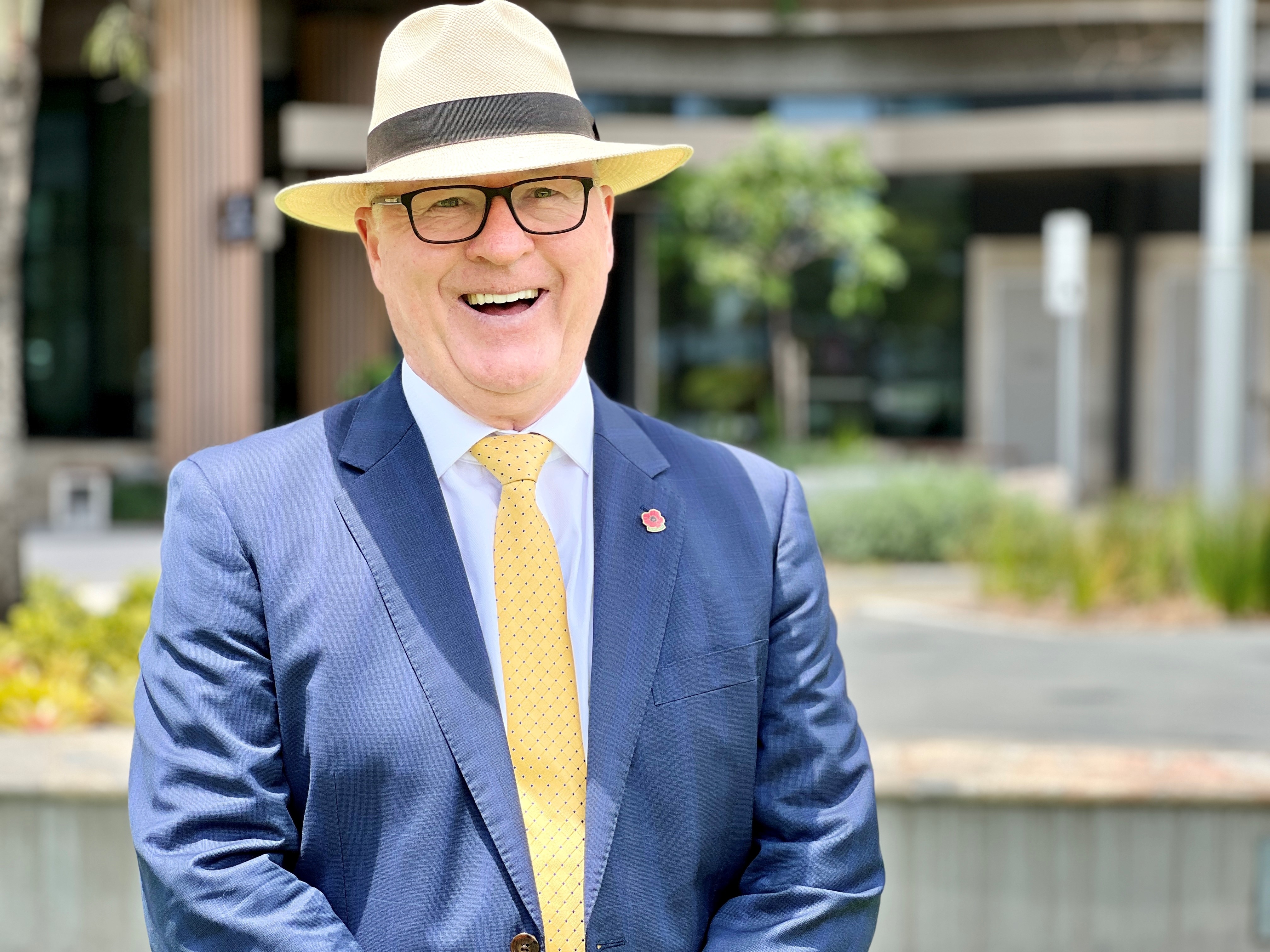 A man in a Panama hat and a suit smiles at the camera.