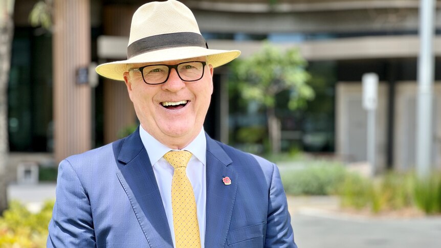 A man in a Panama hat and a suit smiles at the camera.