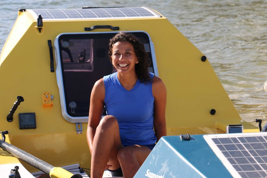 A woman in a blue top sits in a yellow rowing boat.