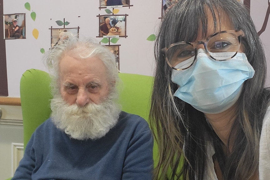 A selfie photo of George Poulos sitting in a green chair, and Litsa Beck in a surgical mask.