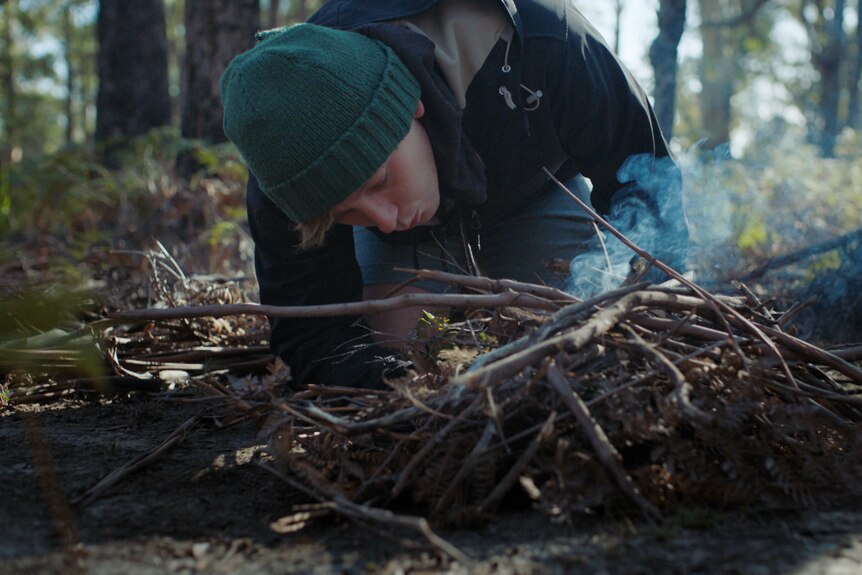 Jamie blowing on a pile of sticks to get them alight