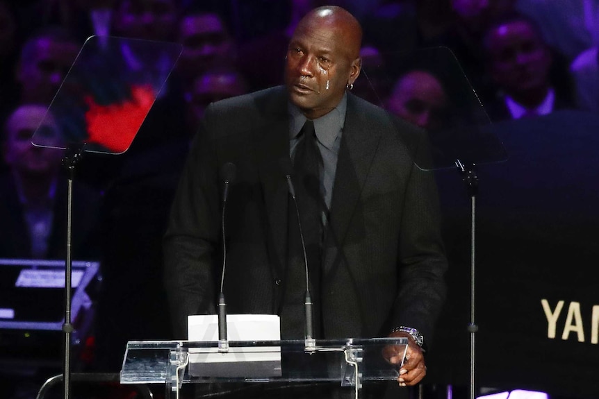 Michael Jordan speaks at a podium. tears visibly run down his cheeks.