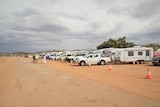 A long line of vehicles towing caravans in a barren camping area.