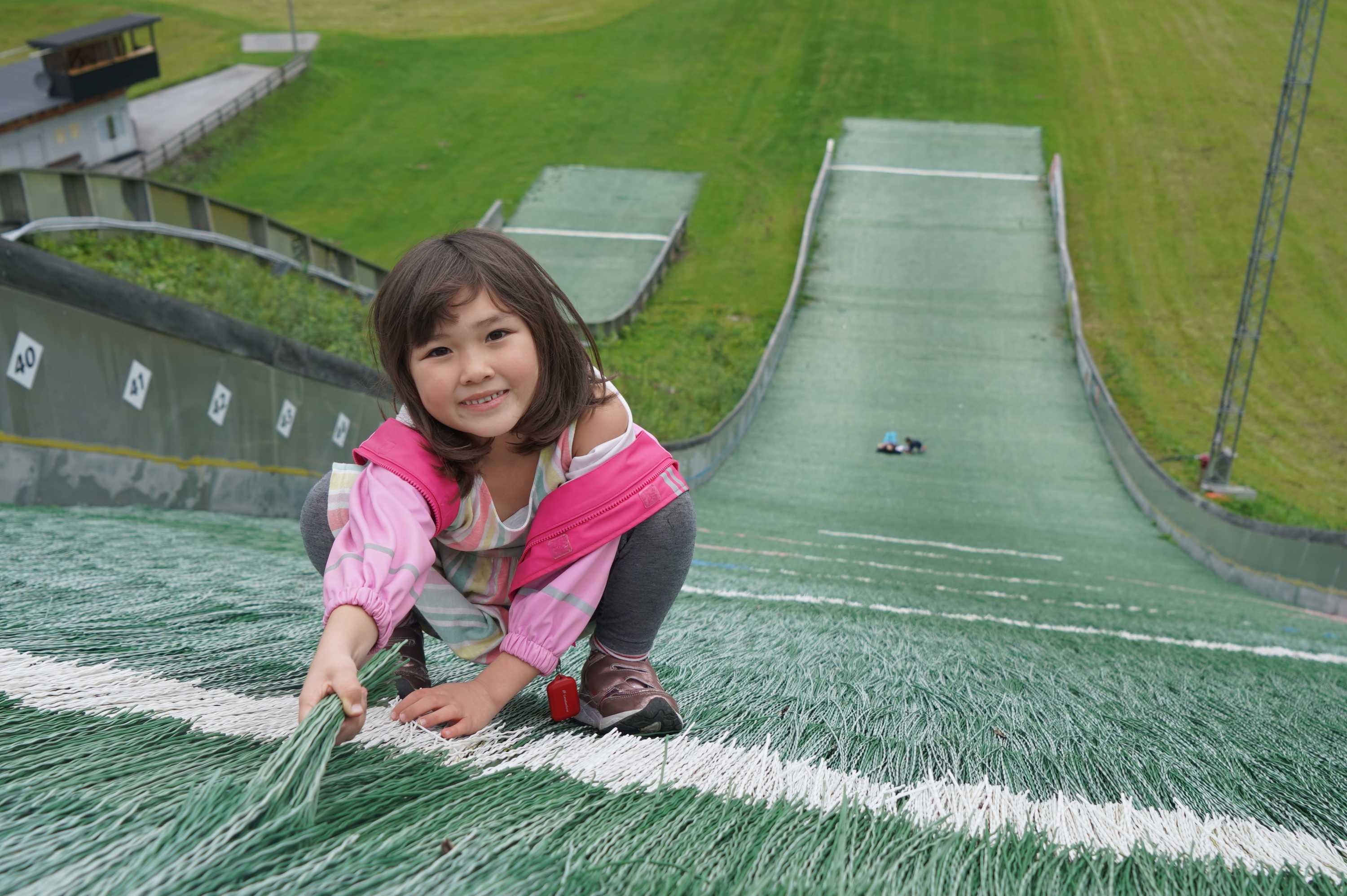 A young girl smiles at the top of a ski slope in summertime.
