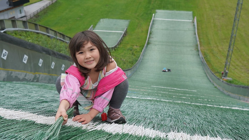 A young girl smiles at the top of a ski slope in summertime.
