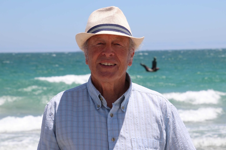 Mike Lefroy stands at a Fremantle beach, in front of a sculpture of CY O'Connor.