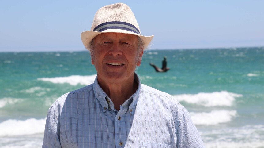 Mike Lefroy stands at a Fremantle beach, in front of a sculpture of CY O'Connor.