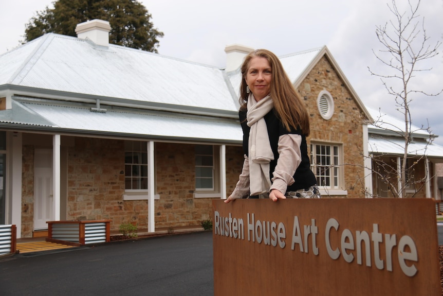 A woman leans against a sign outside an art gallery