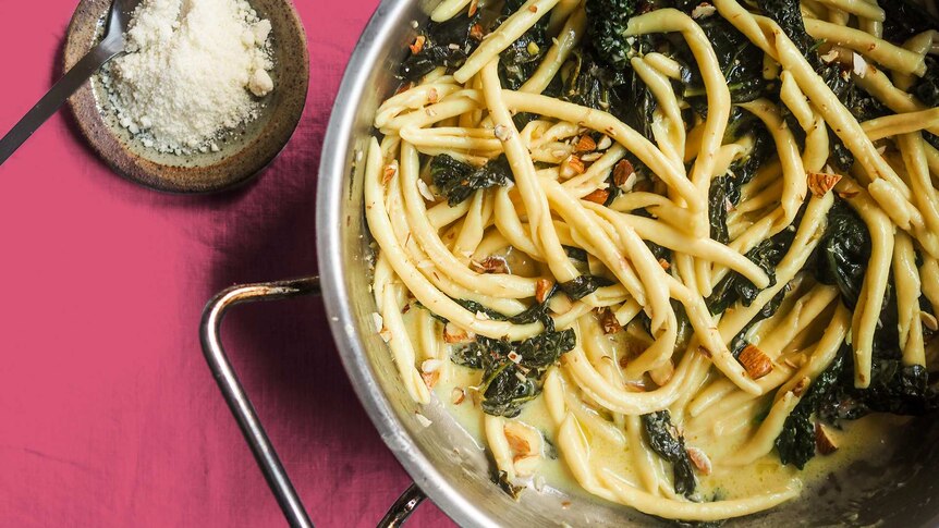 A close up of a pan filled with pasta, kale, cream, lemon and almonds, a quick dinner in one pan.